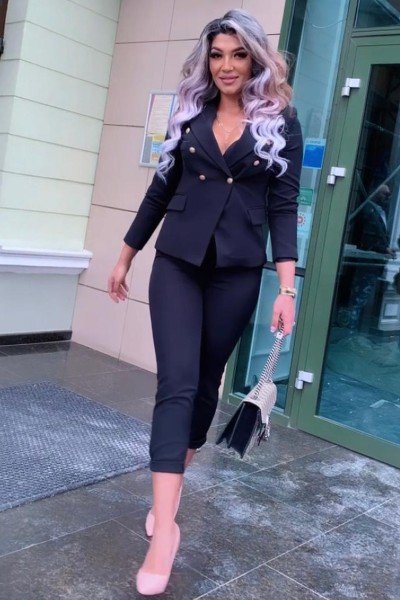 Melisa walking outside in her black outfit and pink heels. She smiles at you.