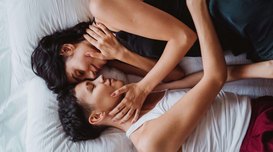 an escort and her client lying in bed stroking each others' cheeks