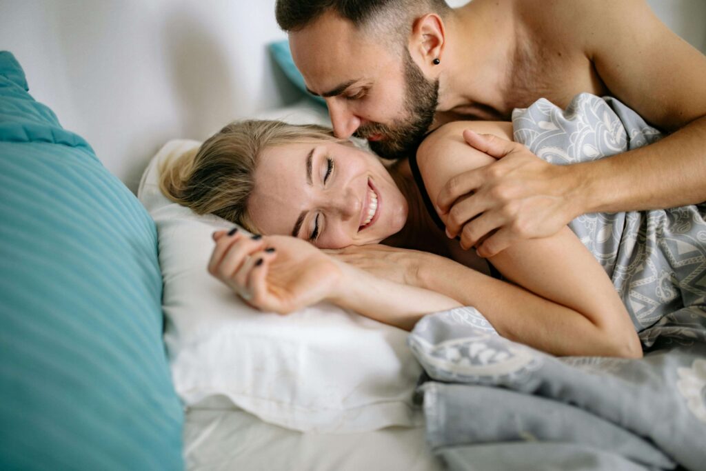 an escort and her client smiling in bed